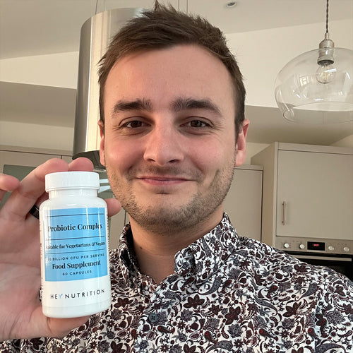 Smiling man in a patterned shirt holding a bottle of Hey Nutrition Probiotic Complex, showing the label with "Probiotic Complex, Suitable for Vegetarians & Vegans, 20 Billion CFU per Serving, Food Supplement, 60 Capsules."