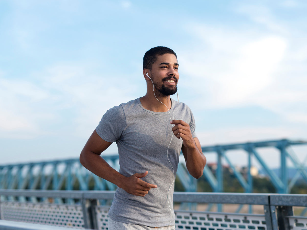 Man jogging outdoors in a grey t-shirt with earphones, looking happy and energized.