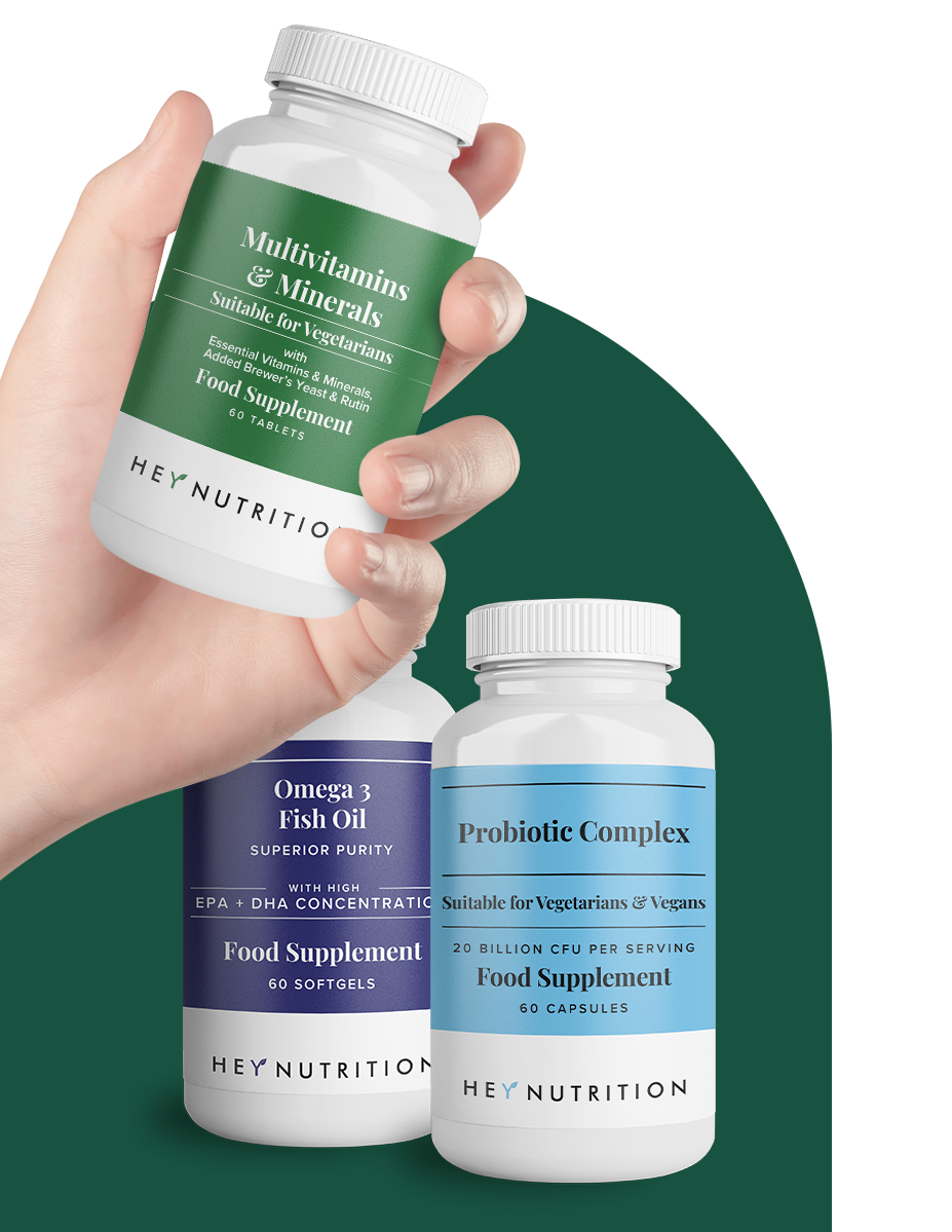 Hand holding a Hey Nutrition Multivitamins & Minerals bottle in front of Probiotic Complex and Omega 3 Fish Oil bottles
