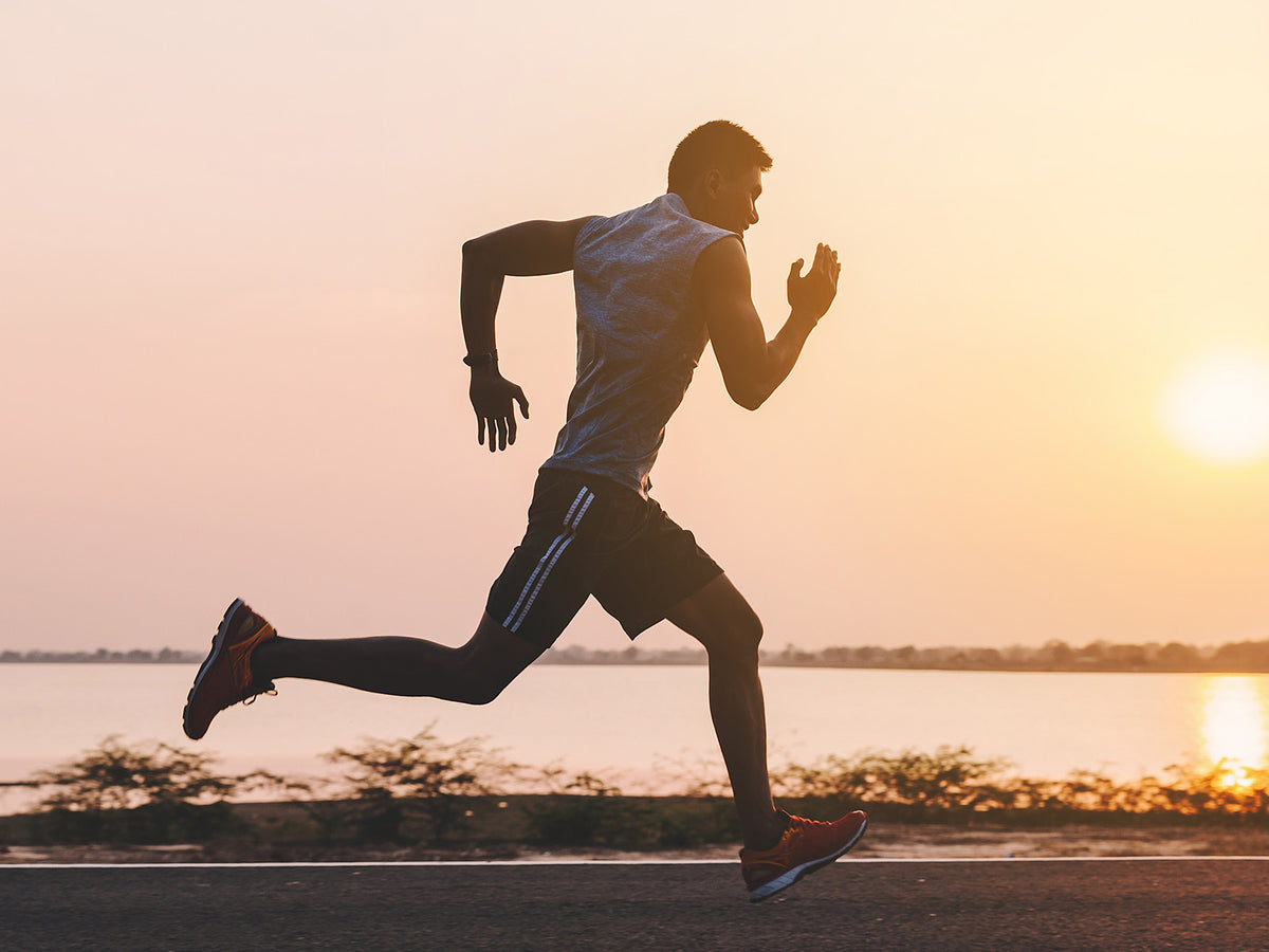 Man running outdoors at sunset near water, demonstrating energy, endurance, and an active wellness routine.
