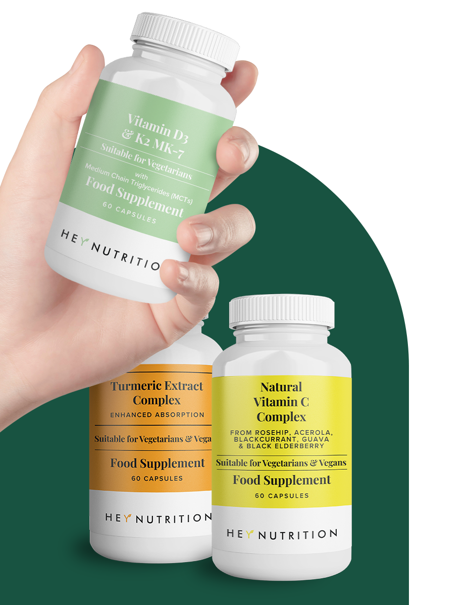 Hand holding Hey Nutrition’s Vitamin D3 & K2 MK-7 supplement bottle with Turmeric and Vitamin C bottles behind, against green background.