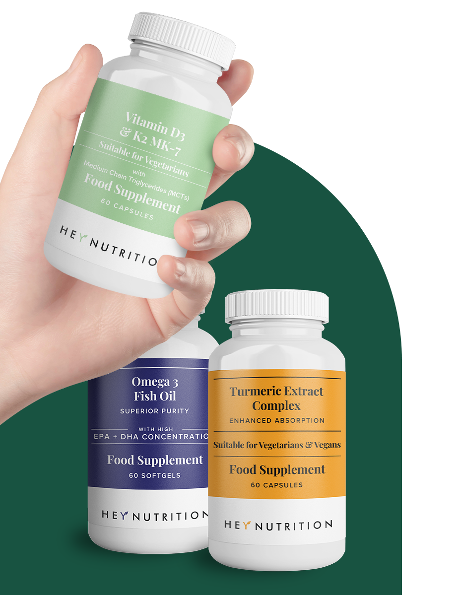 Hand holding a Hey Nutrition Vitamin D3 & K2 MK-7 bottle in the foreground, with Omega 3 Fish Oil and Turmeric Extract Complex bottles slightly behind, showcasing the full supplement range.