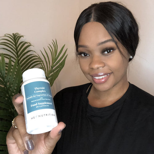 A woman in a black shirt with neatly styled hair smiling and holding Hey Nutrition Thyroid Complex, presenting the thyroid support supplement in a friendly and relatable way.